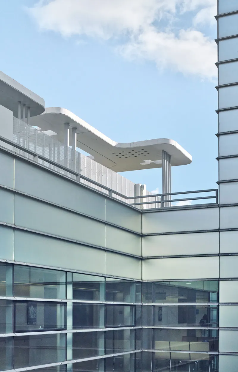 Curved glass facade with horizontal banding and perforated canopy structures on the upper terrace