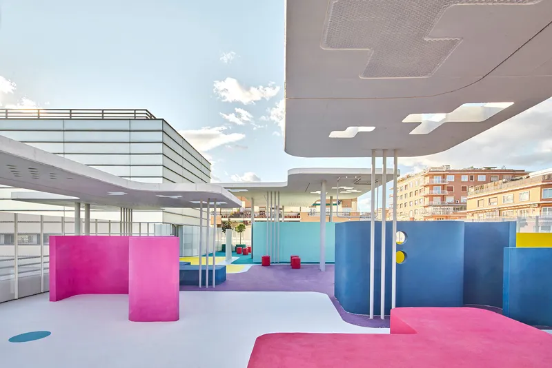 Rooftop terrace with curving pink and blue partitions under a floating concrete canopy in daylight