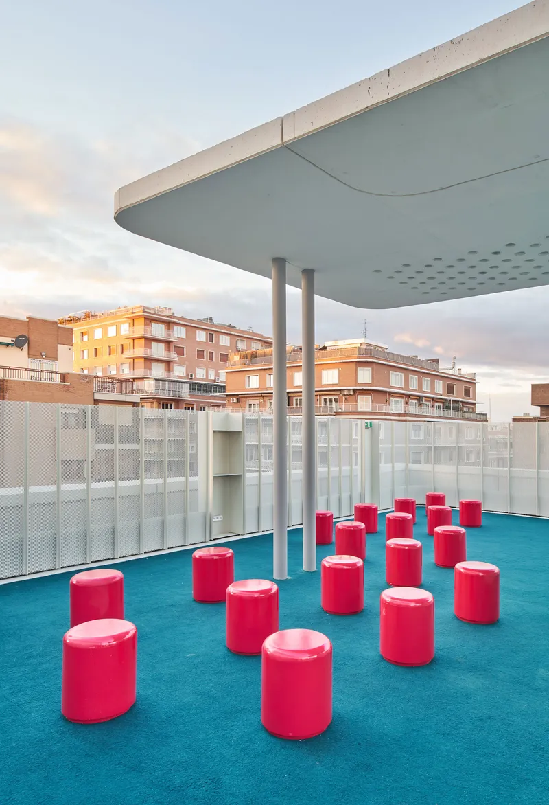 Rooftop deck with red cylindrical stools on turquoise carpet under a curved canopy at dusk