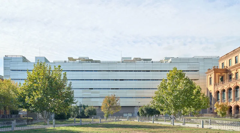 Horizontal louvered facade spanning multiple stories with trees in the foreground and a lawn below