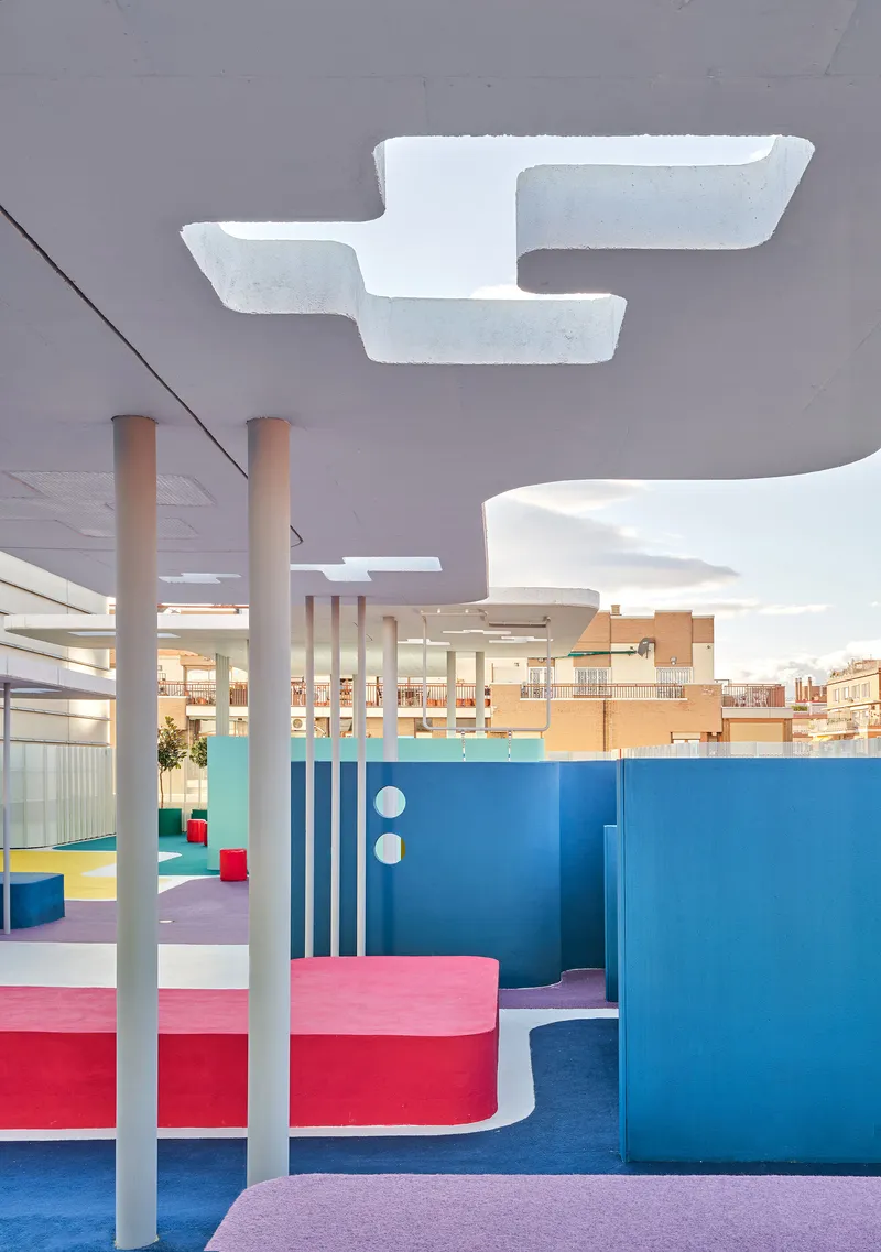 Interior rooftop space with curved colorful seating platforms, white columns, and sculptural ceiling cutouts
