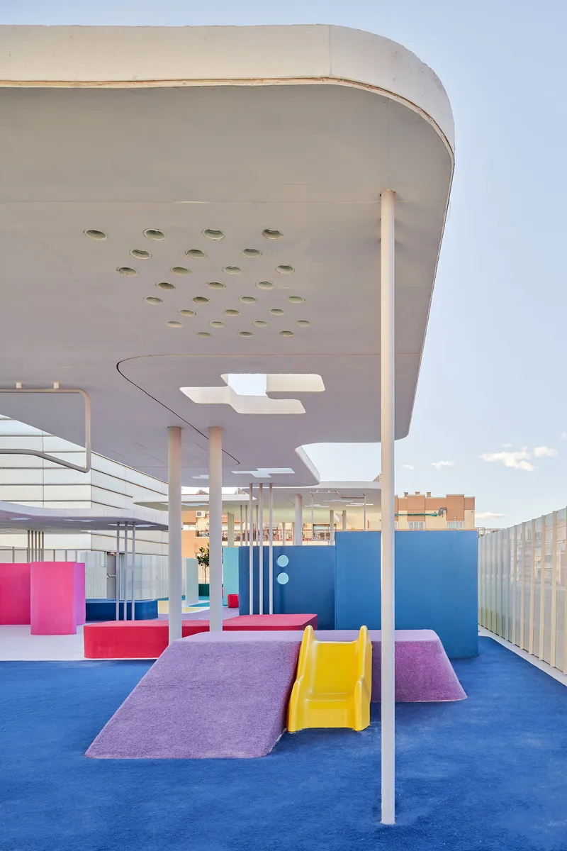 Rooftop play area with curved canopy, perforated soffit, white columns, and blue rubber surfacing with colorful play elements
