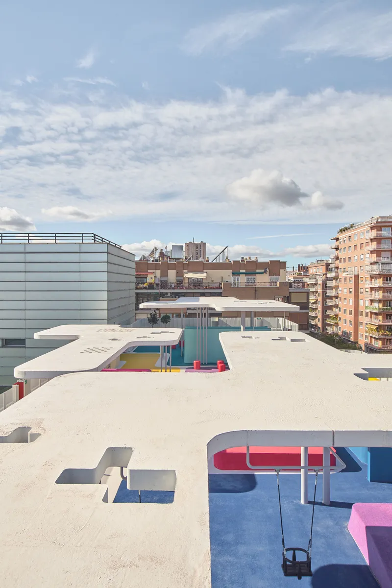 Rooftop terrace with curved canopies, blue rubber surfacing, and scattered play elements against the surrounding cityscape