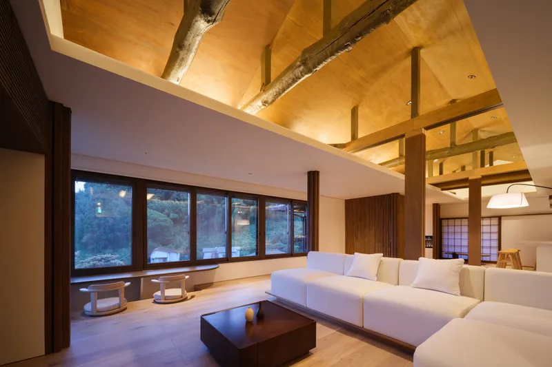 Seating area beneath exposed timber frame with ribbon windows overlooking evening hillside