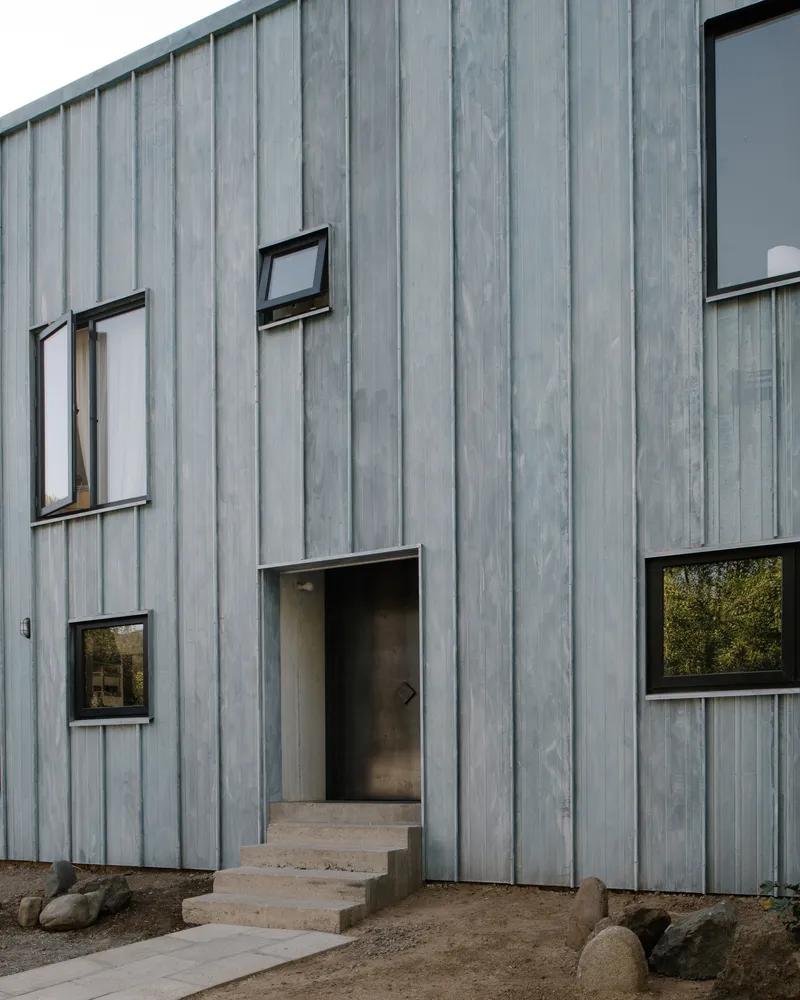 Entry steps leading to recessed doorway in vertical timber cladding with scattered window openings