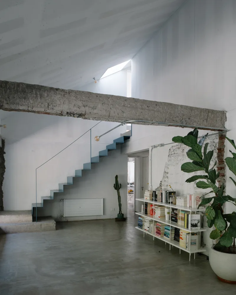 Double-height interior with blue metal staircase, exposed concrete beam, and slanted skylight above