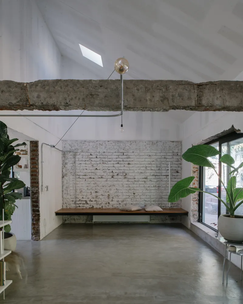 Double-height interior space with exposed concrete beam, whitewashed brick wall and polished concrete floor