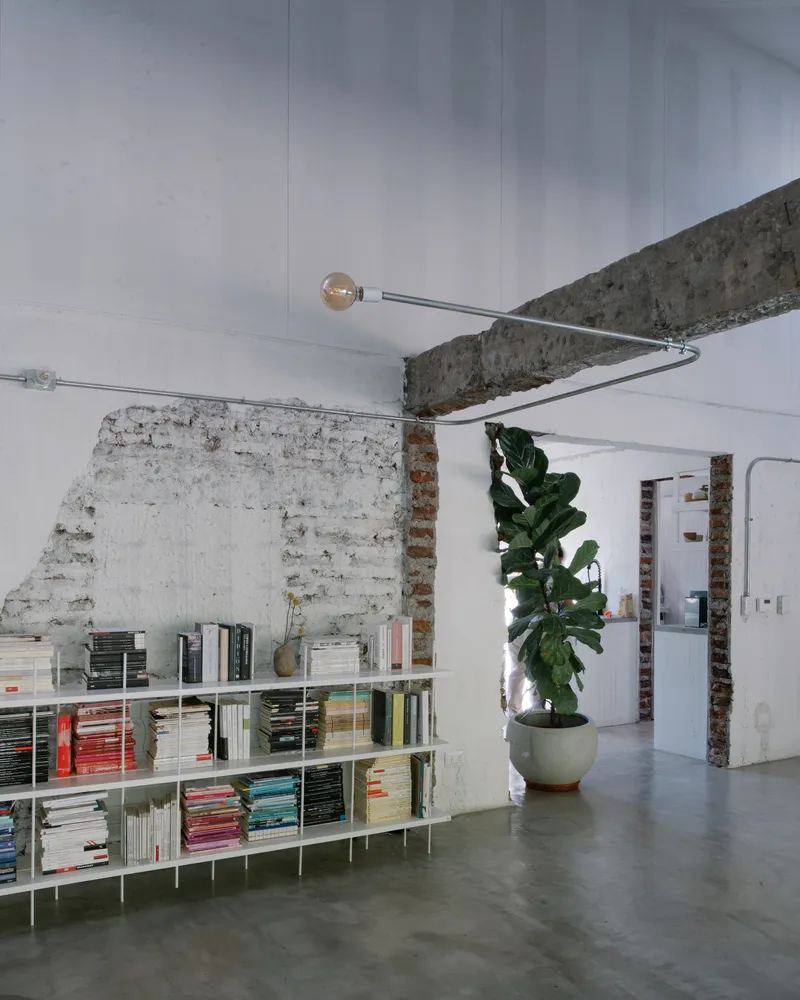 Looking up at exposed concrete beam with pendant light fixture and whitewashed brick partition below