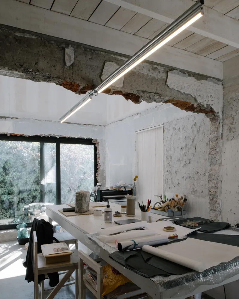 Workshop table beneath linear fluorescent fixture with exposed brick and plaster meeting at the ceiling