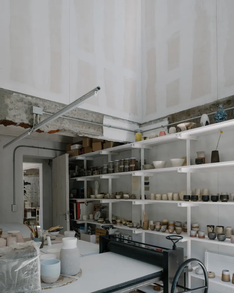 Corner view of the pottery studio with open shelving and kiln beneath draped fabric ceiling