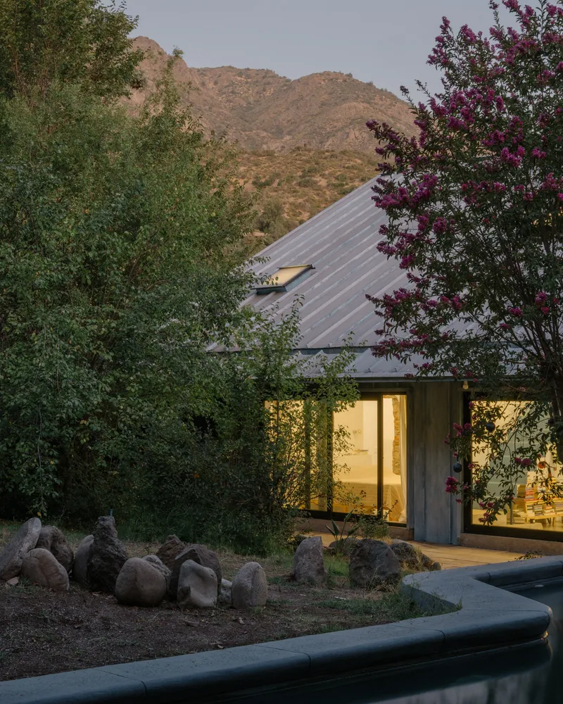 Illuminated studio entrance at dusk with corrugated metal roof and flowering trees against the hillside