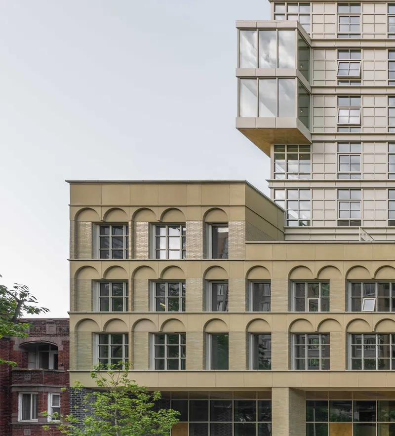 Arched brick facade extending horizontally beneath a projecting glass tower volume