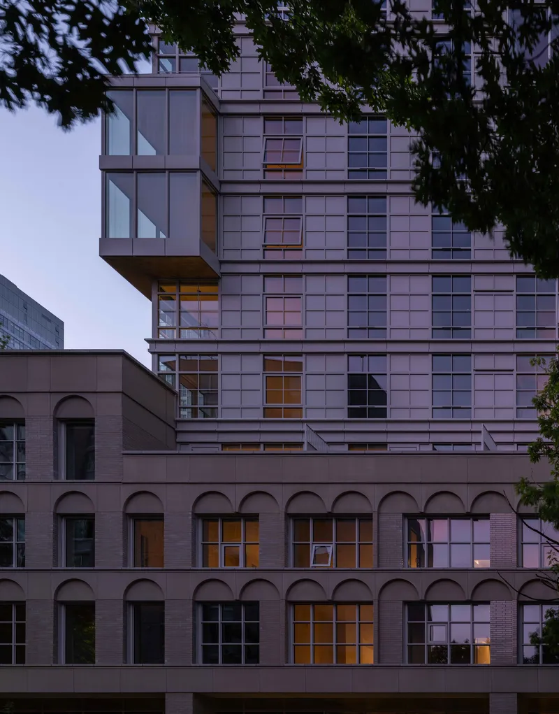 Tower facade rising above a renovated brick structure with arched openings at twilight