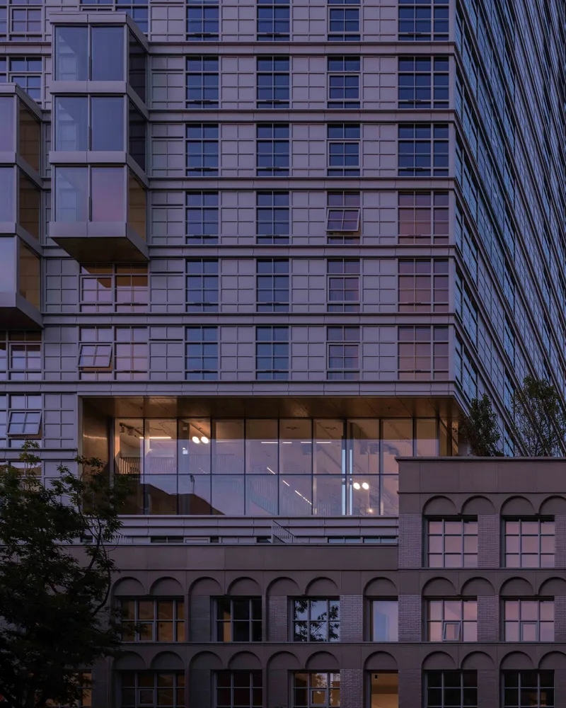 Glass-enclosed lobby bridging the historic brick base and the gridded tower at dusk