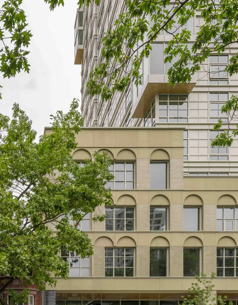 Street view of arched masonry base with tower rising above through green foliage in spring