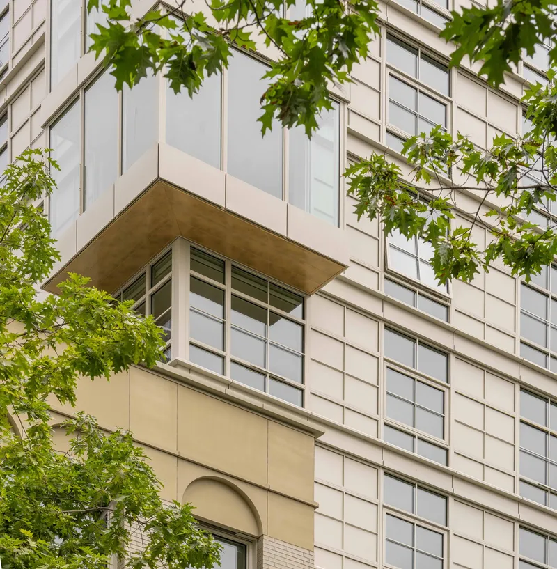 Balcony with timber soffit beneath white panel facade framed by green tree branches