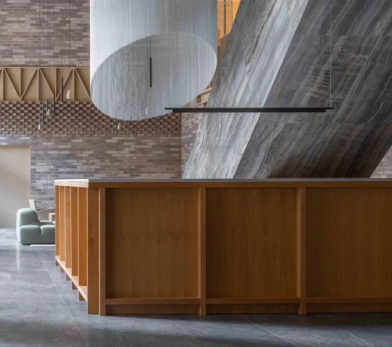 Reception desk with timber paneling below suspended sculptural element and brick wall beyond