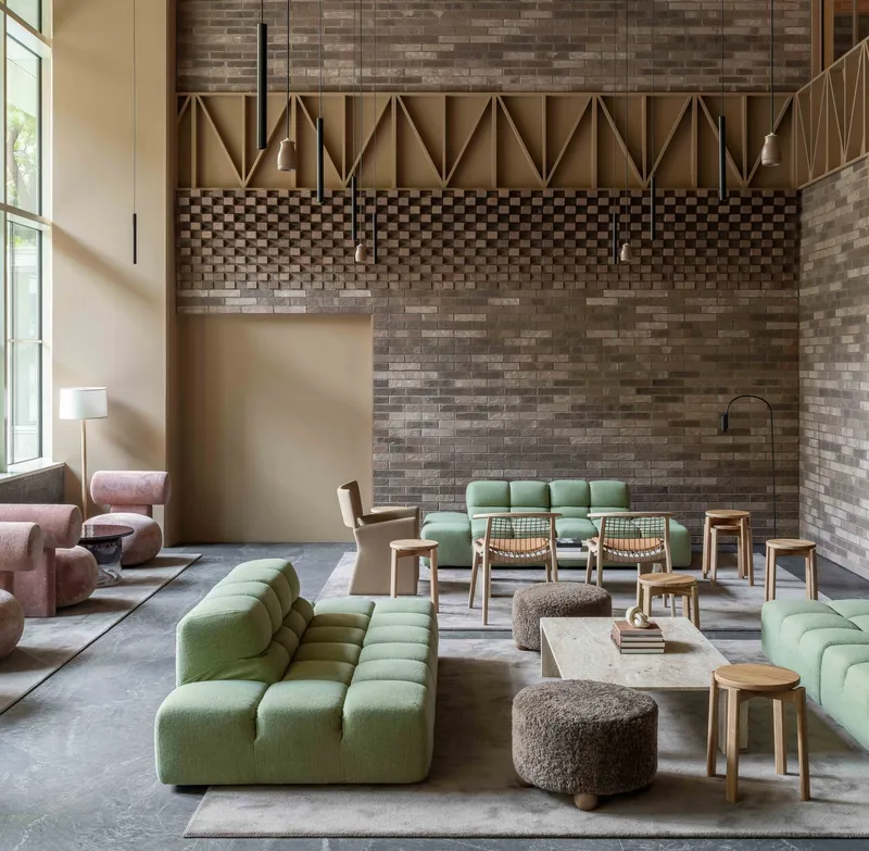 Double-height lounge with variegated brick walls and geometric paneling above green modular seating