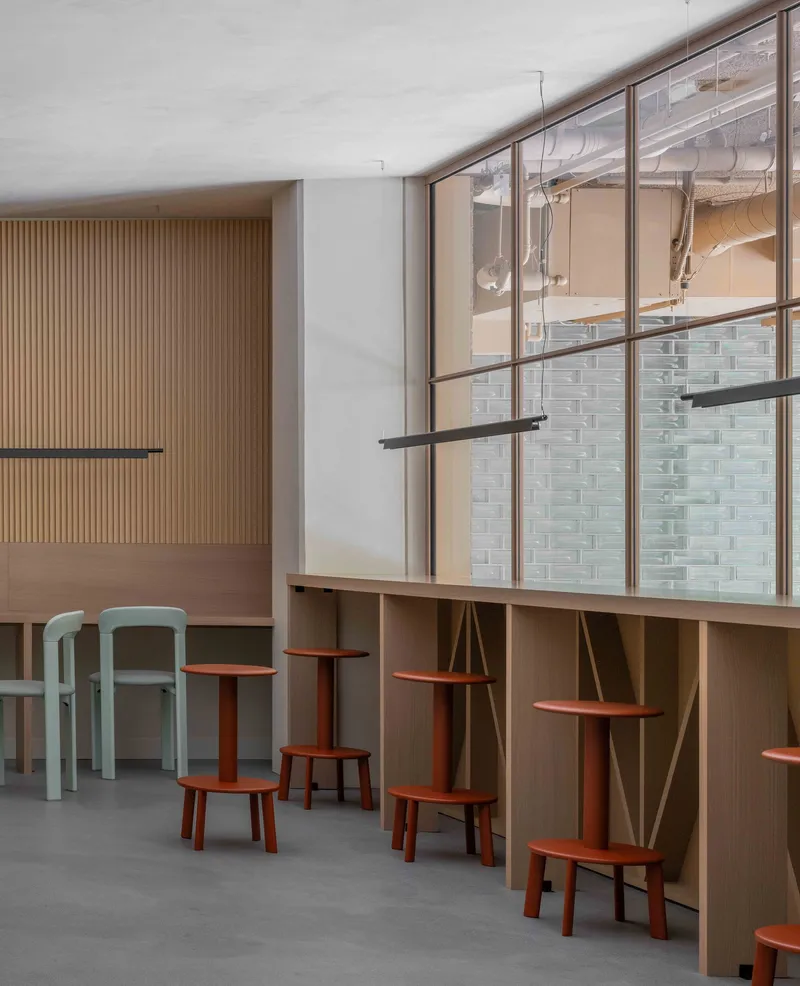 Reading alcove with timber shelving and terracotta stools beneath a window overlooking the brick facade