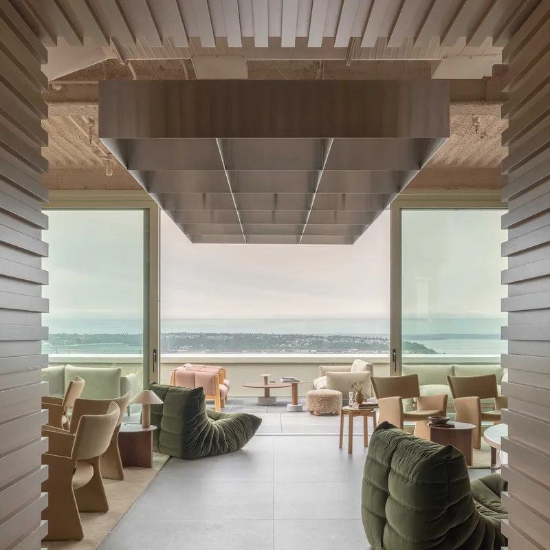 Covered terrace with timber slat ceiling and rammed earth beam framing water views in soft daylight