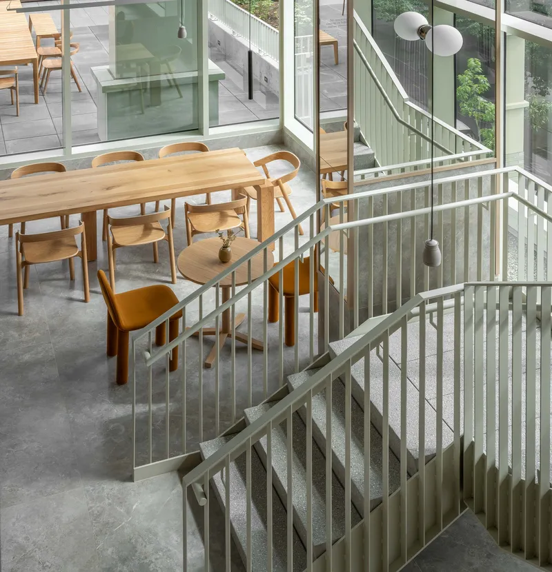 View down pale green metal staircase with vertical bar railings toward dining area and courtyard beyond
