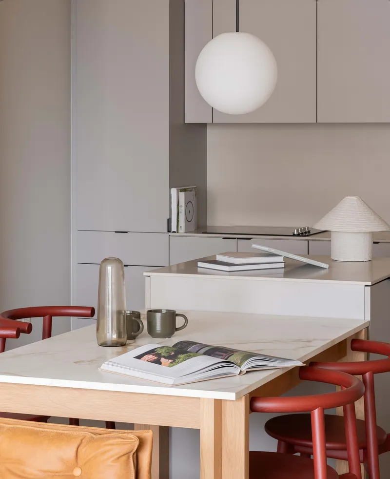 Marble dining table with open magazine, thermal carafe, and red curved stools beneath pendant fixture