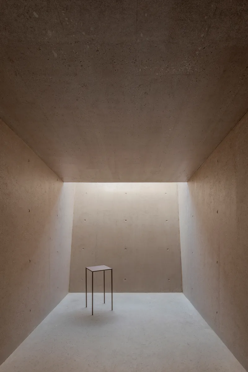Interior gallery space with clerestory lighting and solitary metal table on pale floor