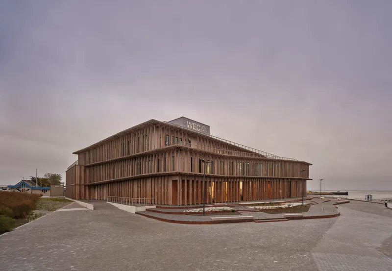 Corner view of the two-story timber screen facade with vertical slats under an overcast sky