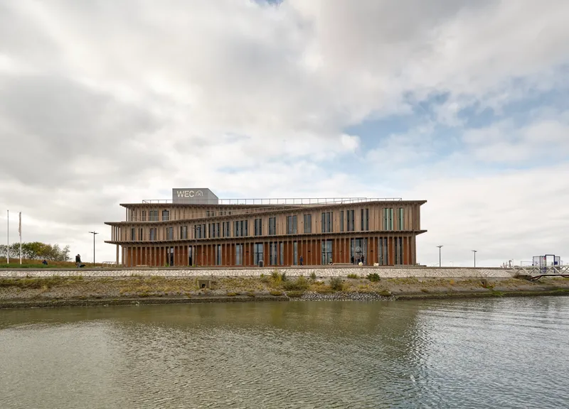 View across the canal showing the elevated building with timber brise-soleil on a stone plinth