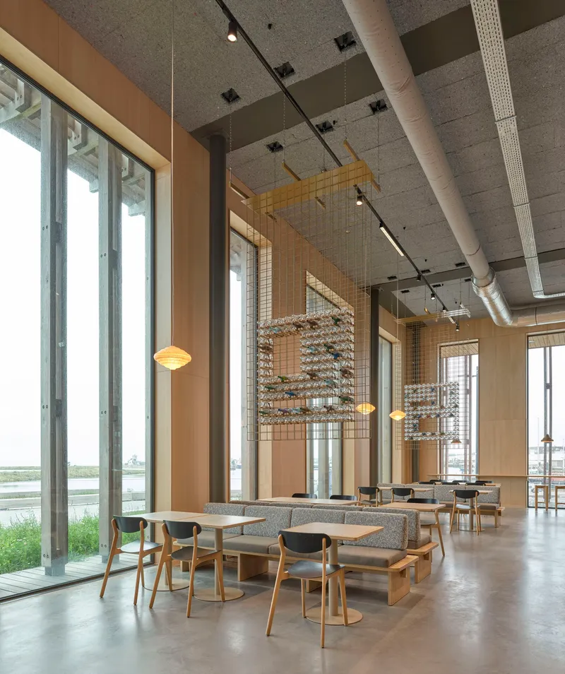 Double-height reading room with timber seating, suspended wire mesh screens and exposed concrete ceiling