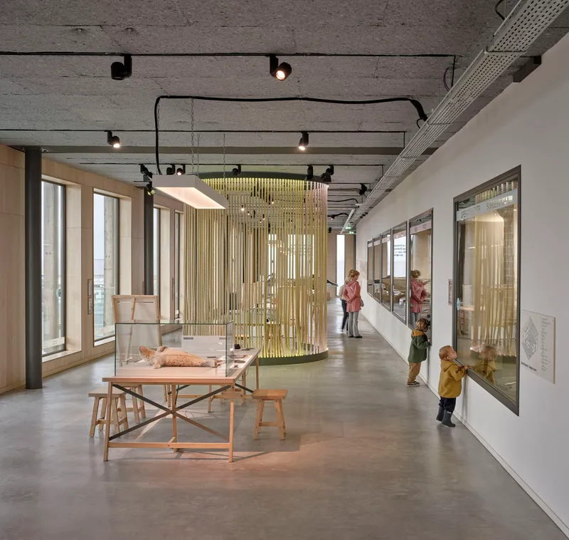 Gallery corridor with suspended brass mesh partition and visitors examining displays along polished concrete floor