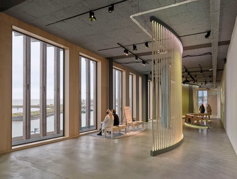 Curved brass bead curtain installation beside tall timber-framed windows with person seated near waterfront view