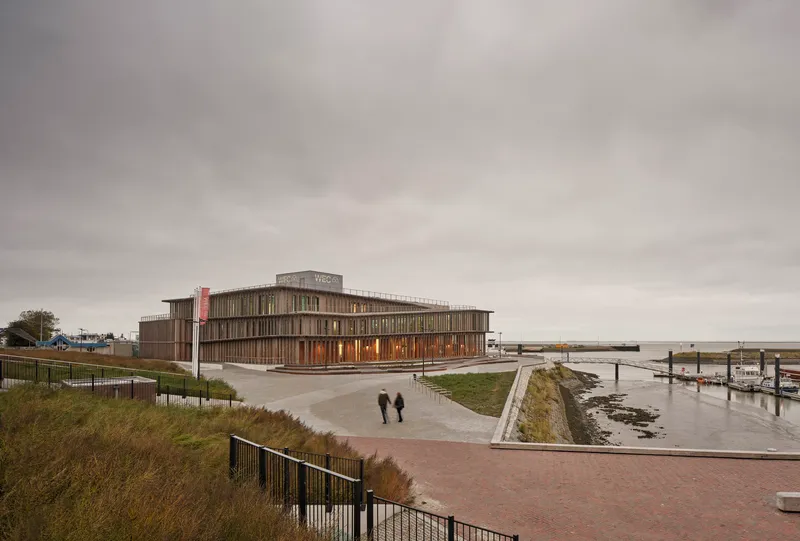 Low angled view of the vertically slatted timber facade with two figures walking the waterfront path