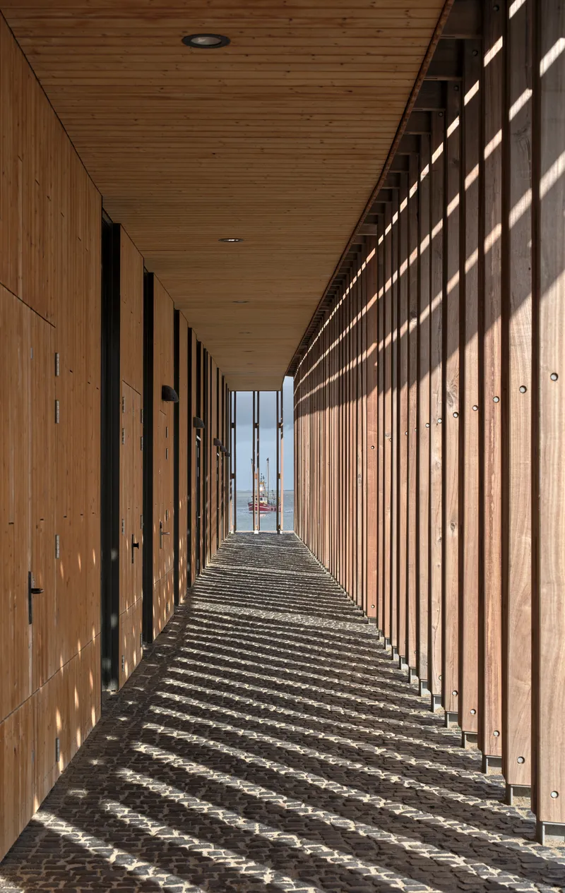 Timber-lined corridor with vertical slat screen casting shadow stripes on the polished floor in bright sunlight