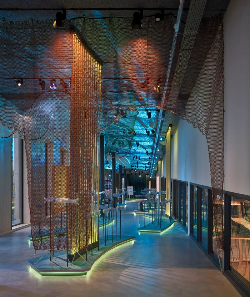 Mirrored ceiling reflecting illuminated brass mesh screens and walkway between glass display cases at twilight