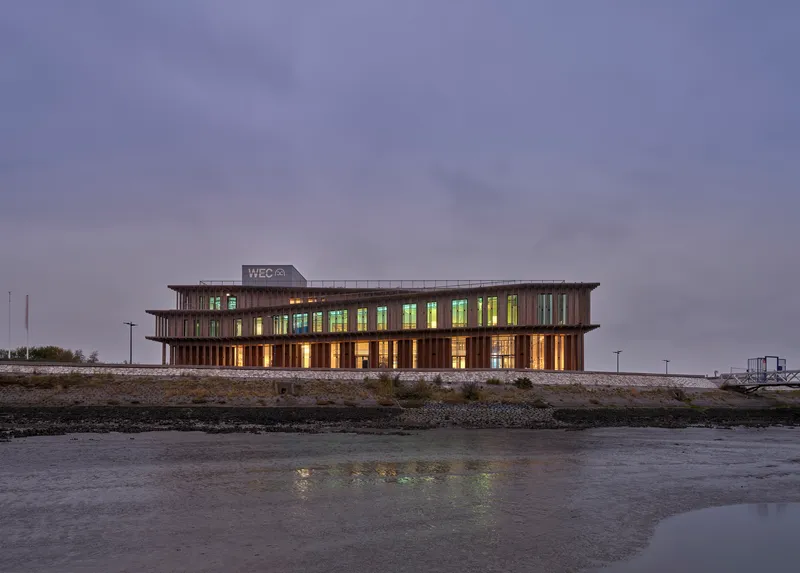 Timber-louvred facade with illuminated interiors viewed from the waterfront at dusk
