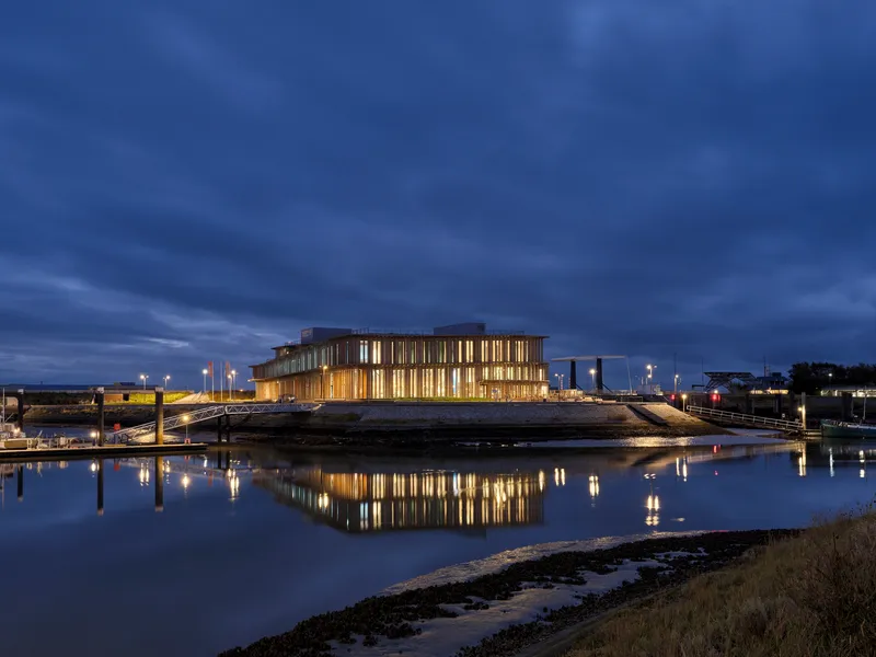 Illuminated building reflecting in calm tidal waters under evening sky with clouds
