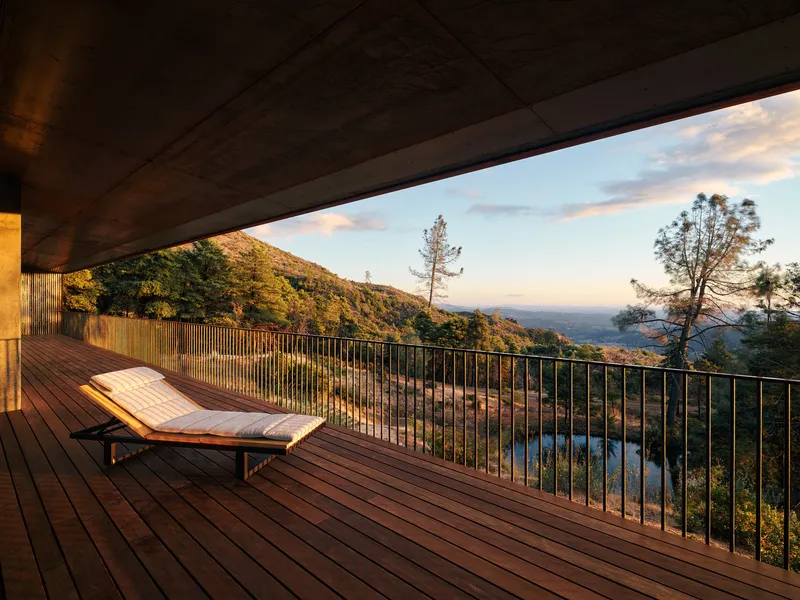 Covered timber deck with lounge chair and metal railing overlooking forested hills at sunset