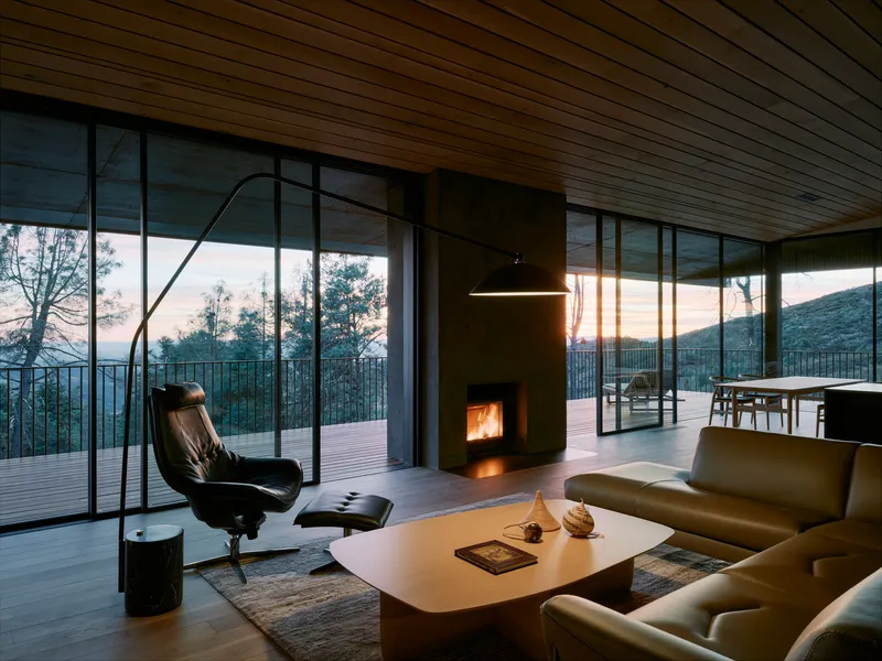 Living room with fireplace and floor-to-ceiling glazing opening to deck at twilight