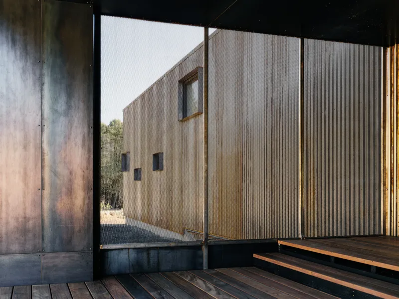 View through sliding glass door to corrugated metal courtyard wall with weathered steel panels flanking the opening