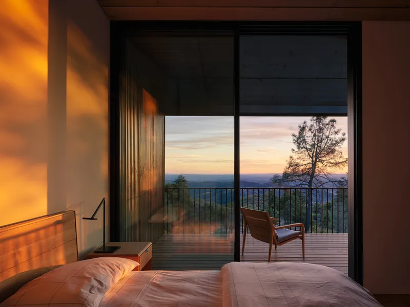 Bedroom with glazed doors opening to a timber deck overlooking distant hills at sunset