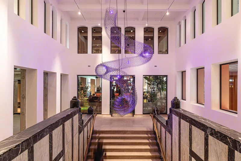 Double-height atrium with purple mesh sculpture suspended from the ceiling and timber stair railings