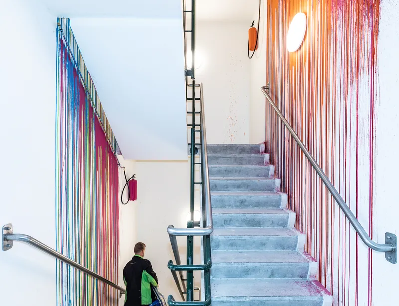 Concrete staircase with steel handrails and multicolored cord installation cascading down white walls as person descends