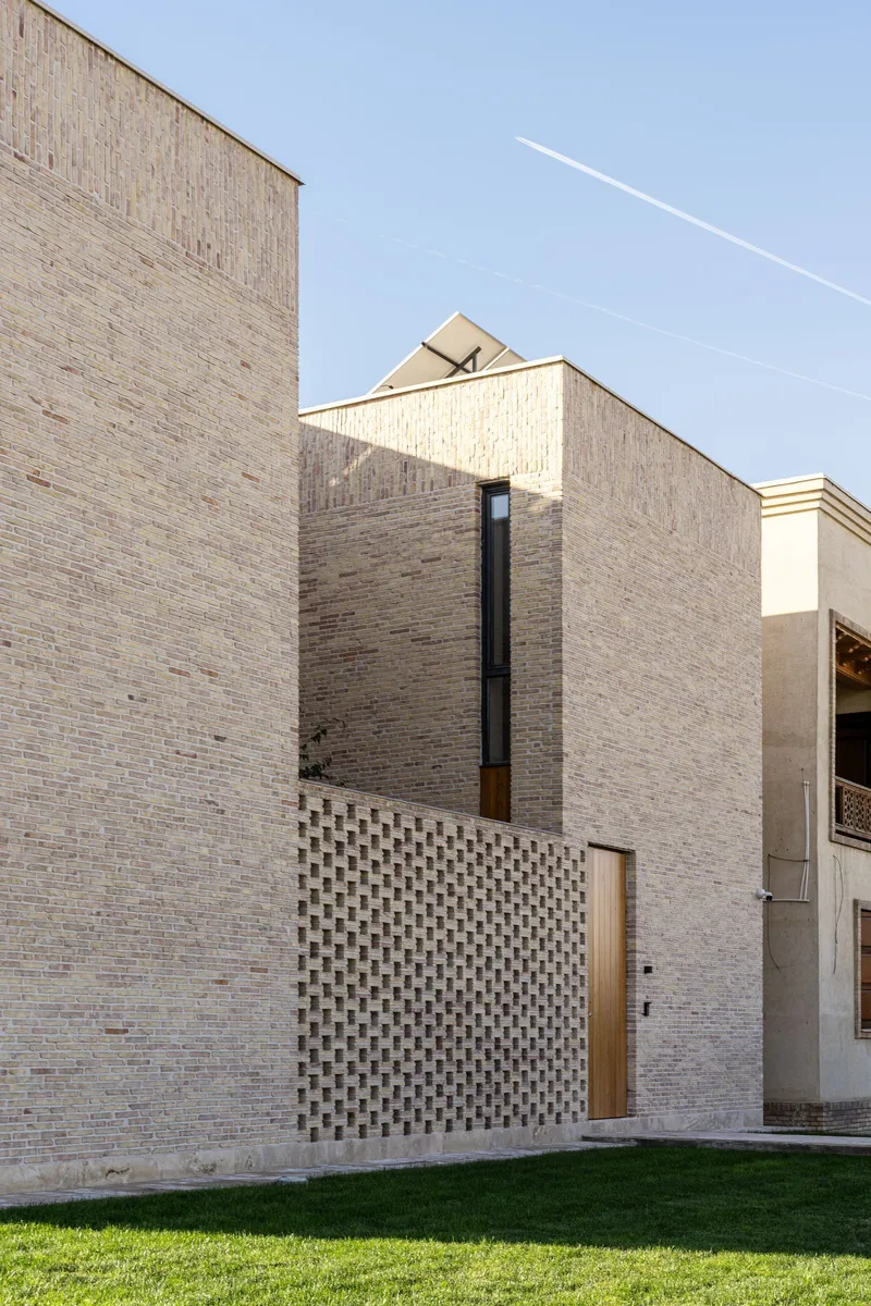 Pale brick volumes with a vertical window and perforated brick screening at ground level