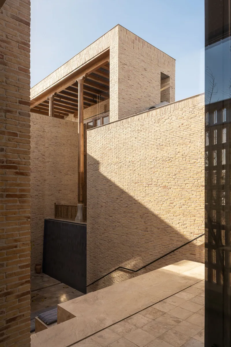 Courtyard view showing exposed timber rafters and brick walls casting diagonal shadows in sunlight