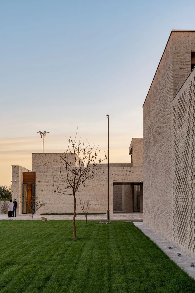 Courtyard view with patterned brick volumes, lawn, and young trees at dusk