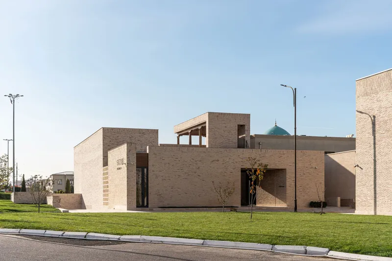 Street view of the layered brick volumes with timber pergola and young trees on lawn