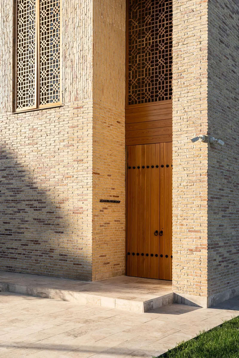 Tall wooden entrance door set within buff brick walls with decorative lattice screens above