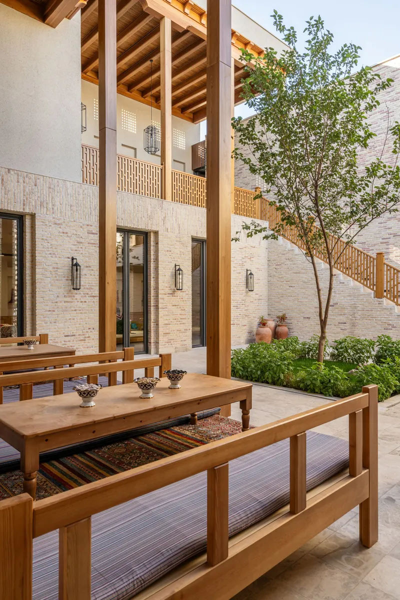 Interior courtyard with timber columns, exposed rafters, wooden benches and a planted tree