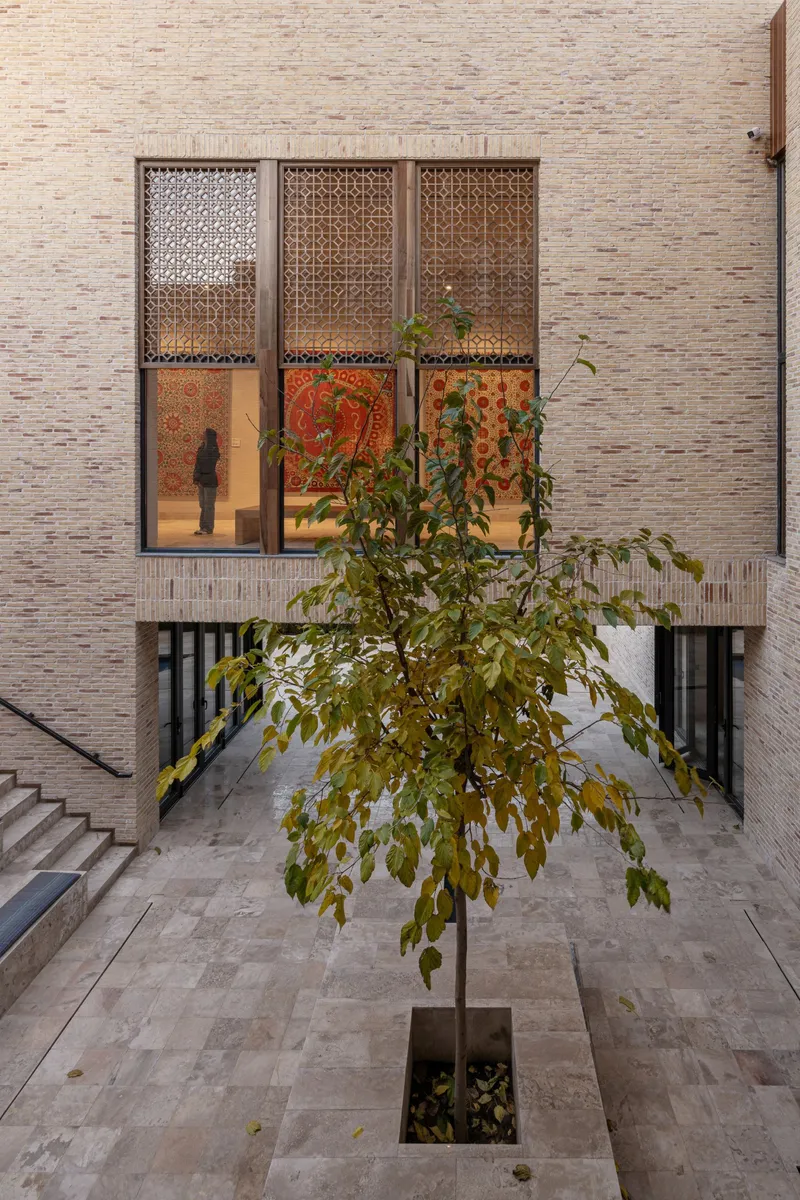 Courtyard with central tree framed by tall openings with patterned screening and decorative tapestries visible inside